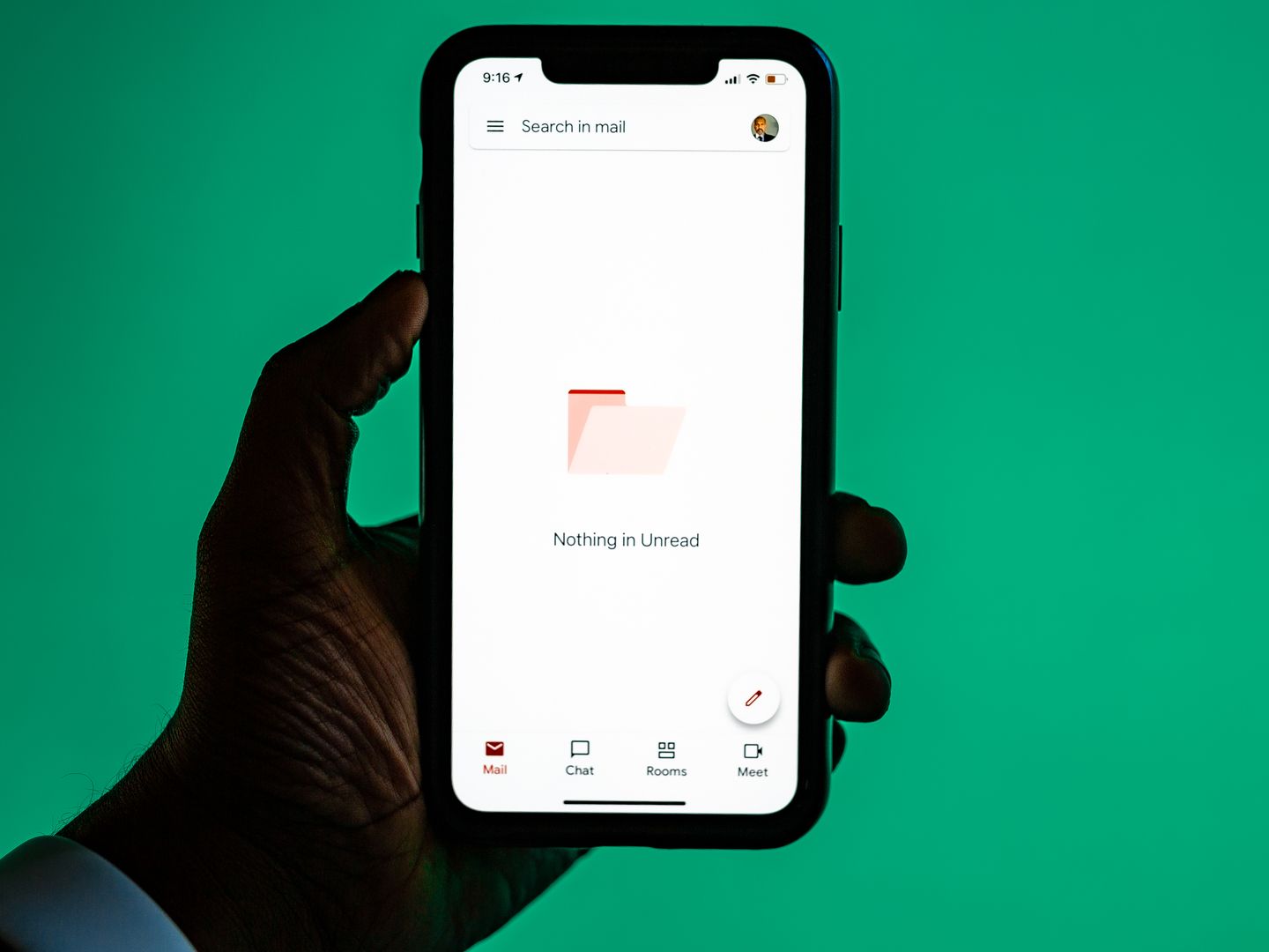 Close up of a hand holding a smartphone displaying email app against a green background.