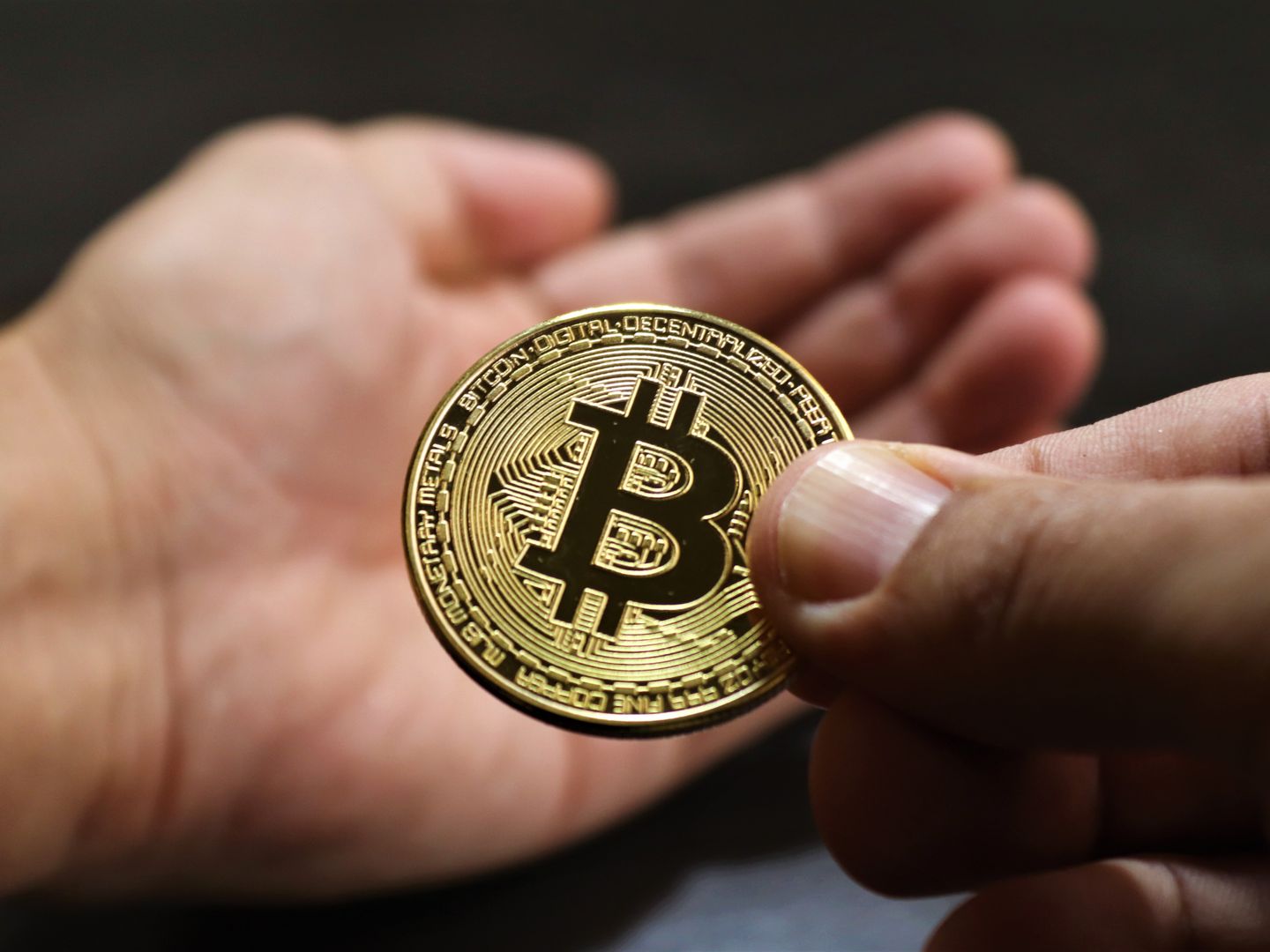 Close up image showing hands exchanging a Bitcoin coin, symbolizing cryptocurrency transactions.