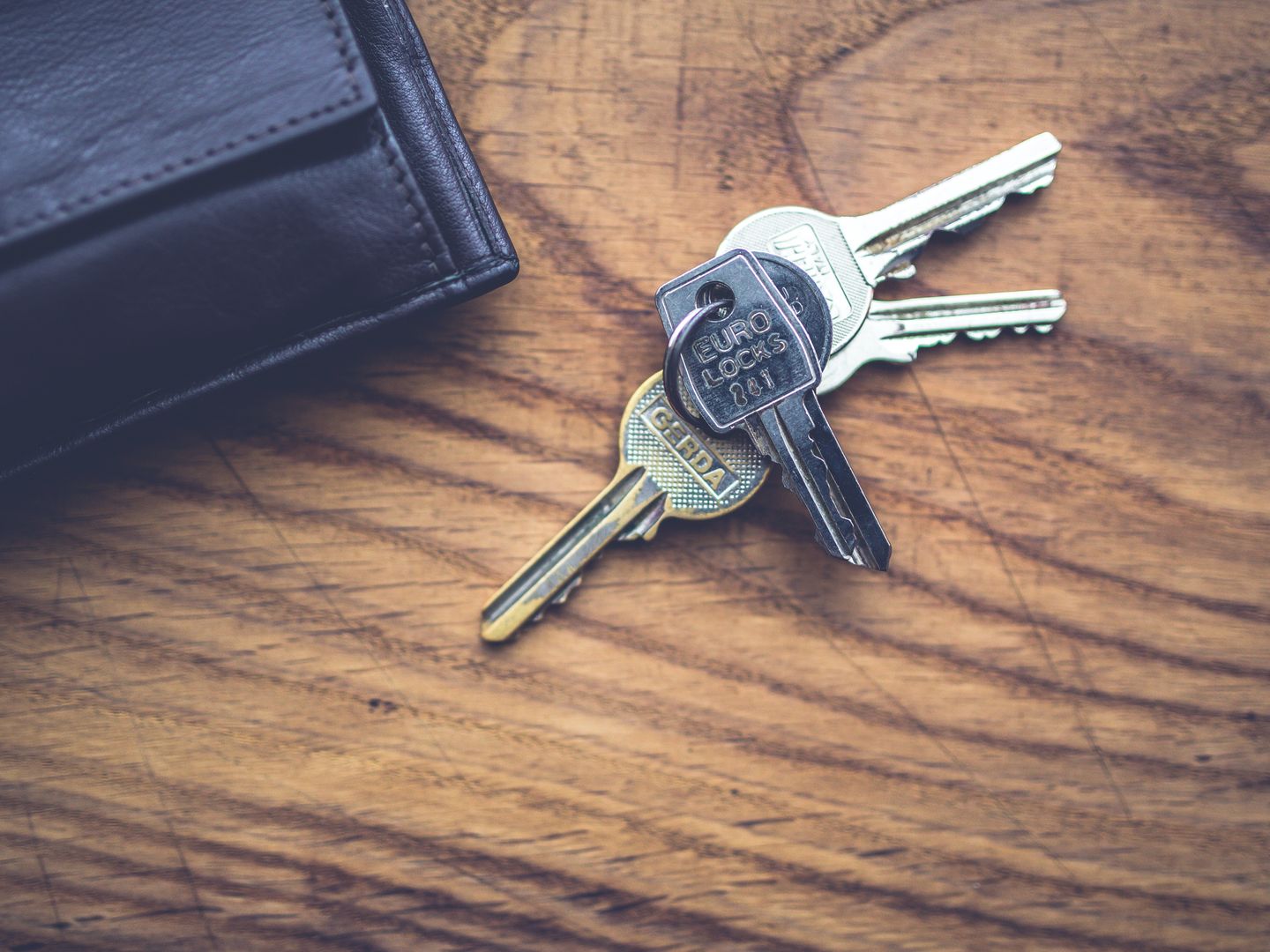Black wallet and metal keys resting on a textured wooden table.