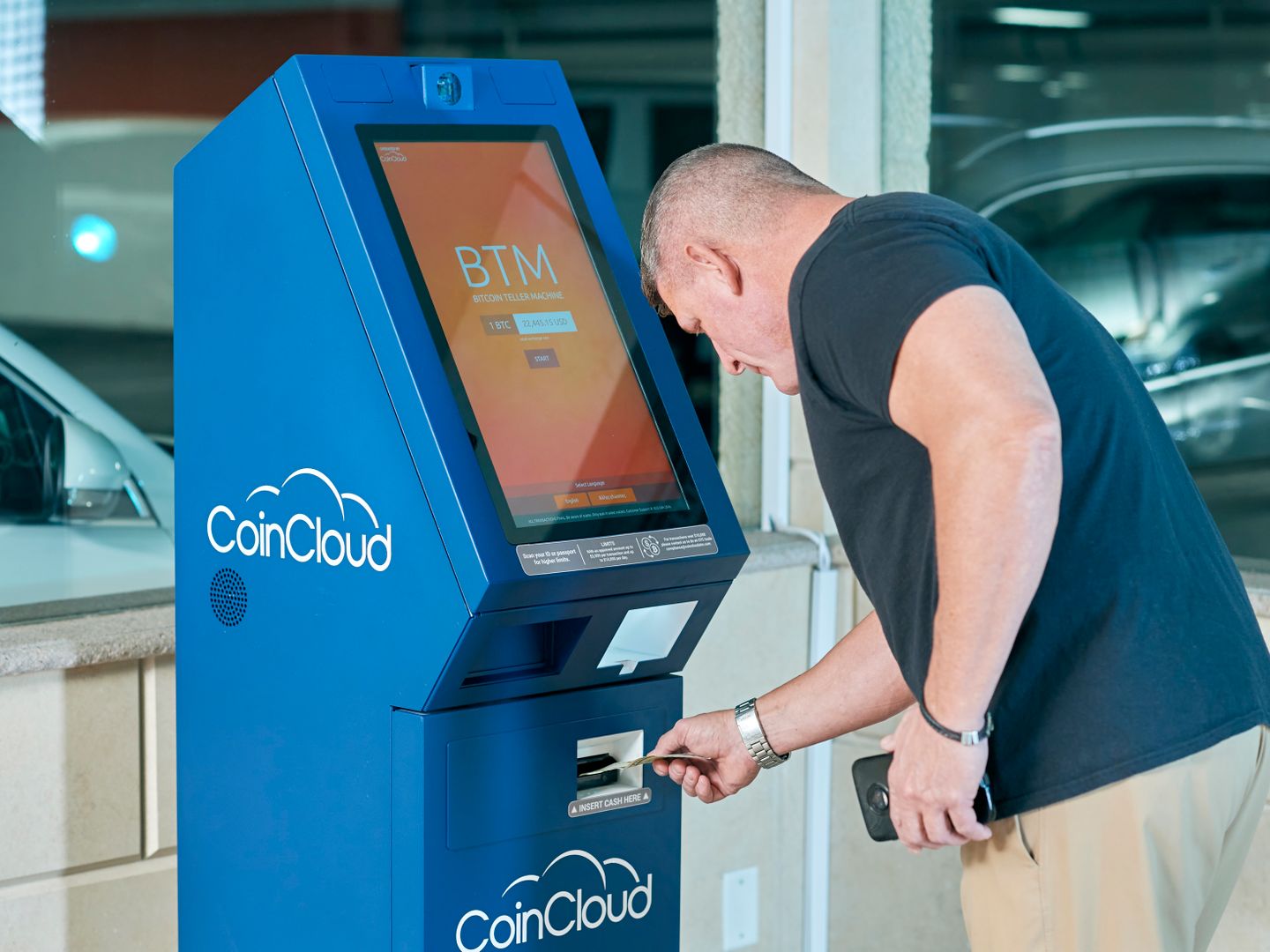 A man interacts with a CoinCloud Bitcoin ATM indoors, making a cryptocurrency transaction